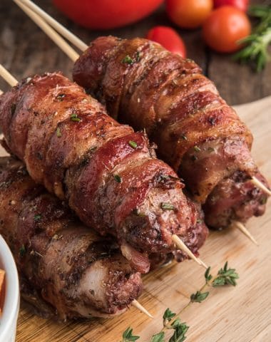 Bacon wrapped beef skewers on a wooden board.