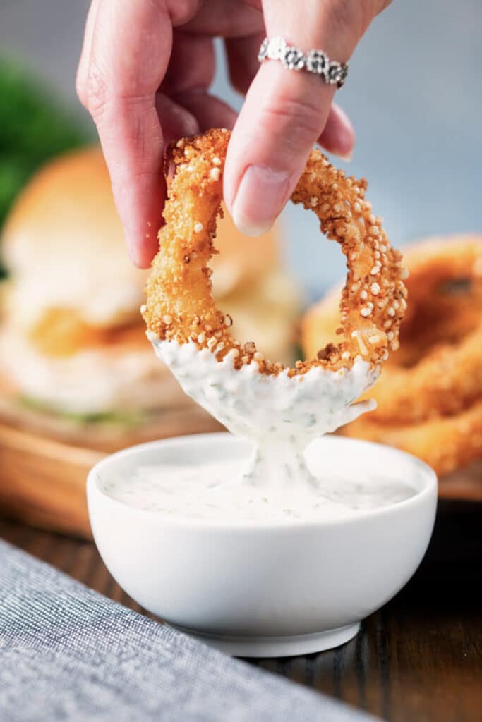 Dipping an onion ring in a dip in a small bowl.