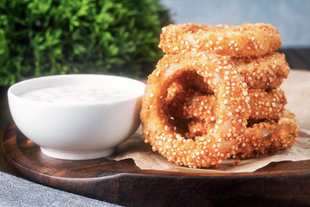 Four onion rings stacked and one leaning against them. Dip in a bowl.